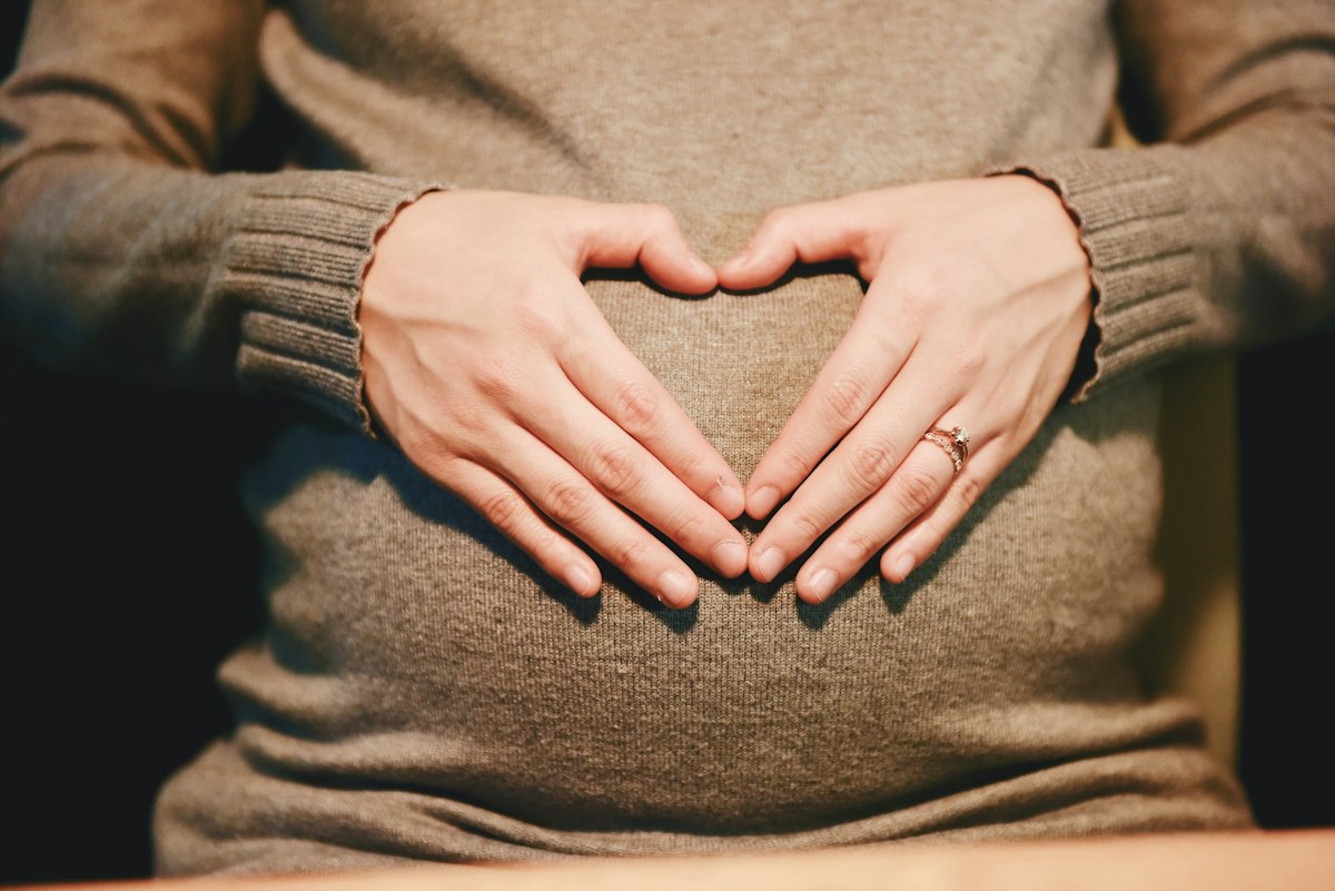 Eine schwangere Frau formt mit ihren Händen ein Herz auf ihrem Babybauch