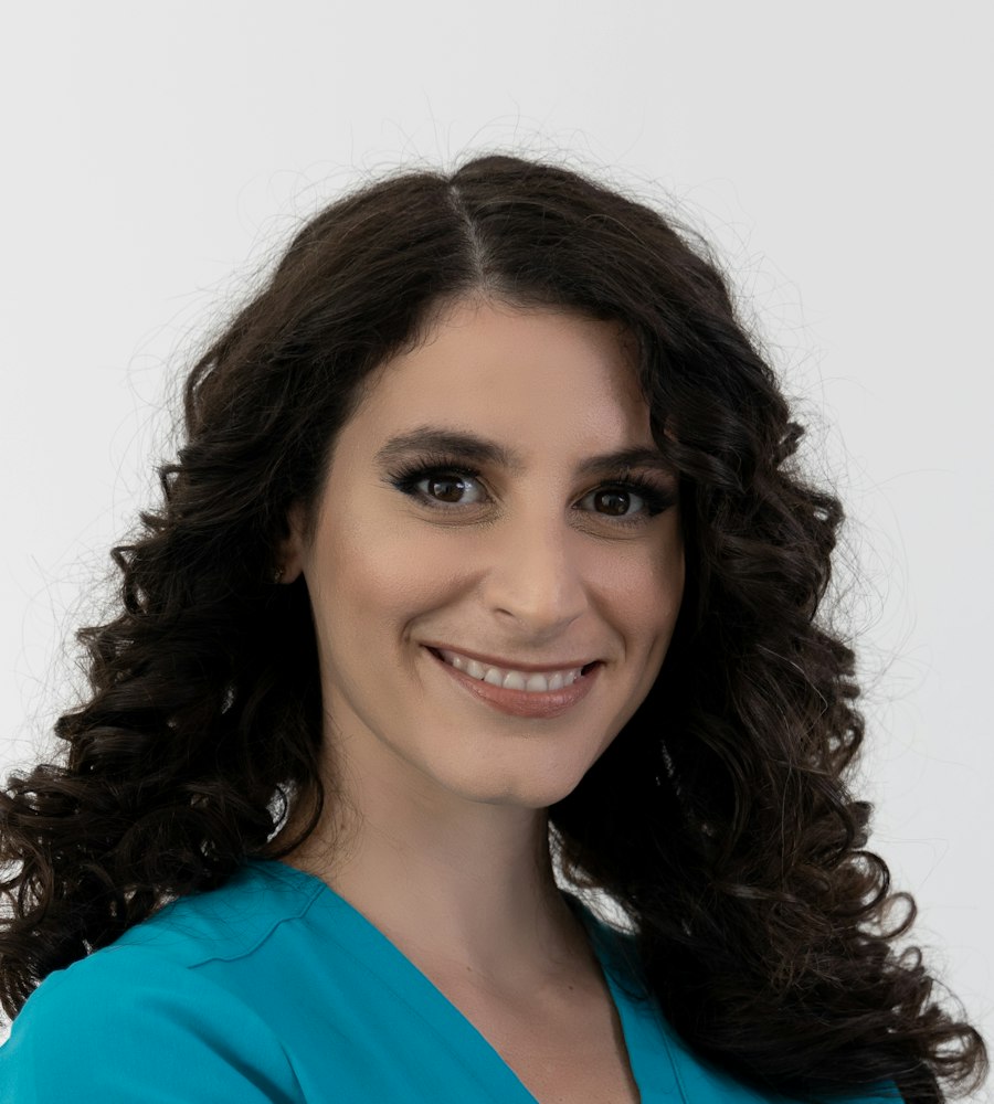 Porträt von Hebamme Anna Müller: eine lächelnde Frau mit dunklen Locken in türkisfarbener Berufskleidung